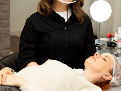 A permanent make-up specialist in a beauty salon prepares the client for the procedure. The master is wearing a special protective mask for working in covid conditions